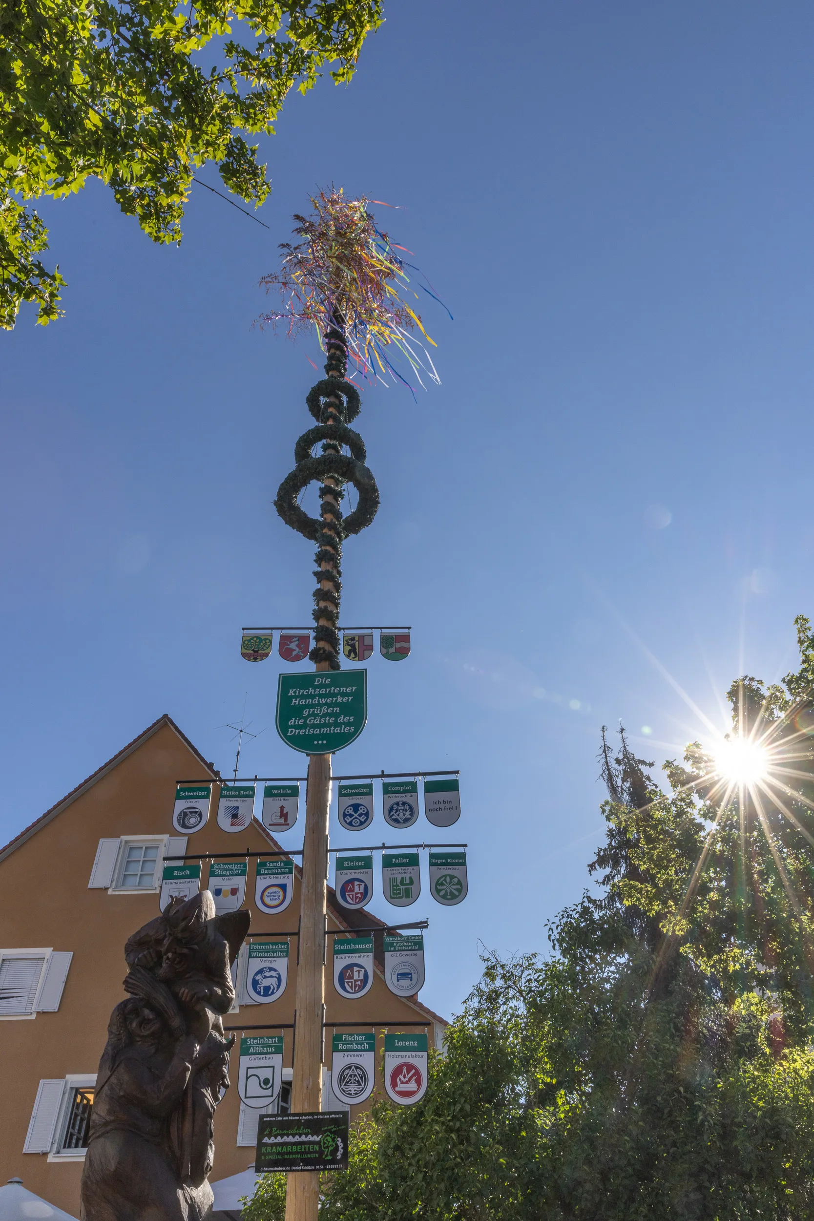Kirchzartener Maibaum an einem sonnigen Tag mit den Wappenschildern der ortsansässigen Handwerksbetriebe, darunter das Schild von Sanda.