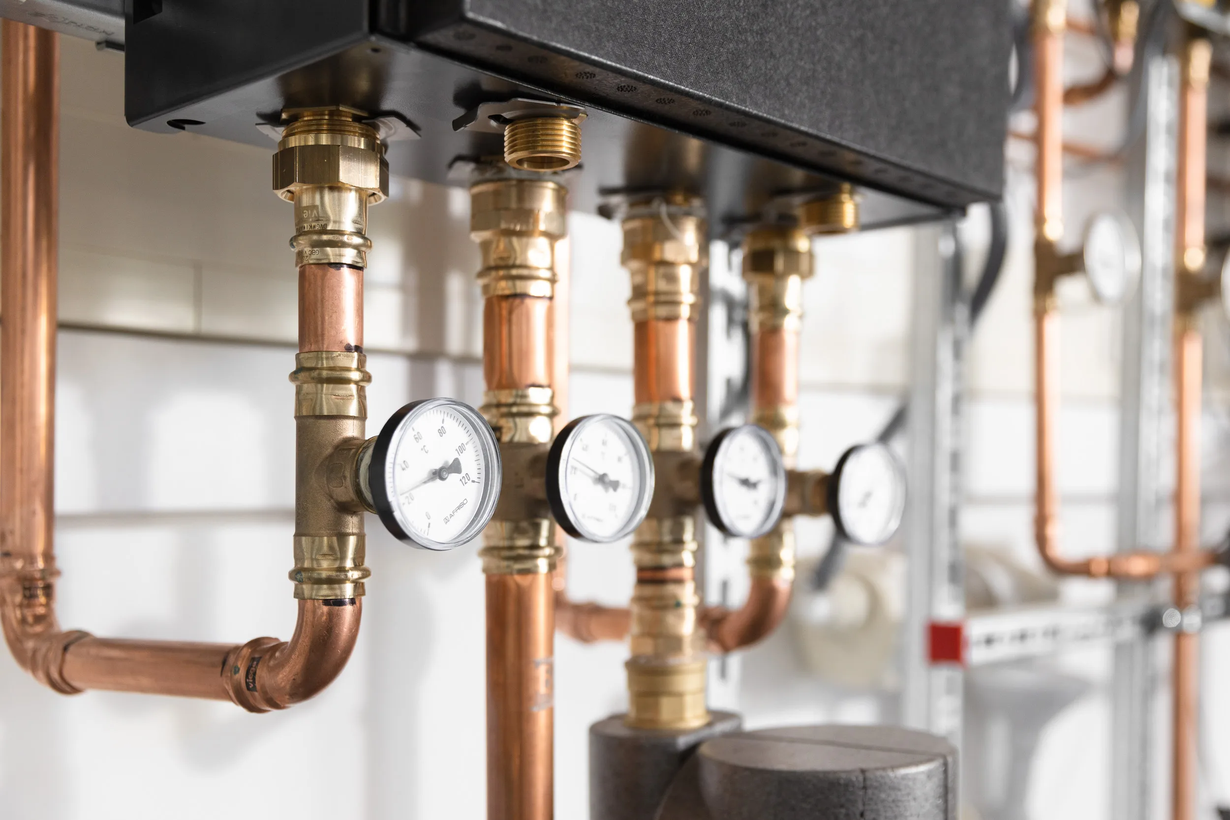 Nahaufnahme einer Heizungsinstallation mit sauber verlöteten Kupferrohren, Messinganschlüssen und vier analogen Temperatur- und Druckmanometern.