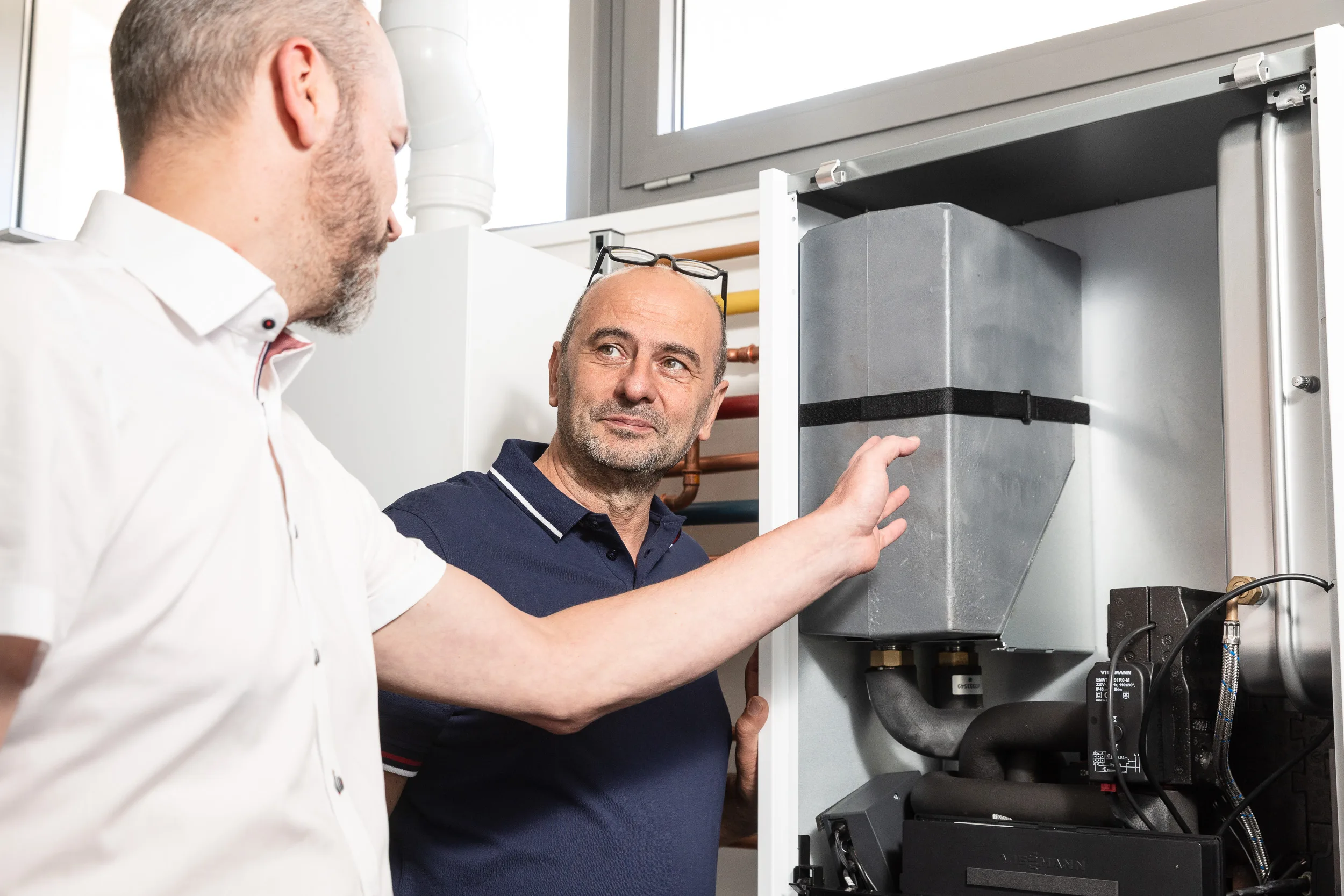 Beratungsgespräch vor einem geöffneten Viessmann-Wandgerät: ein Fachmann erklärt einem Interessenten die Bauteile im Inneren des Brennwertgeräts.