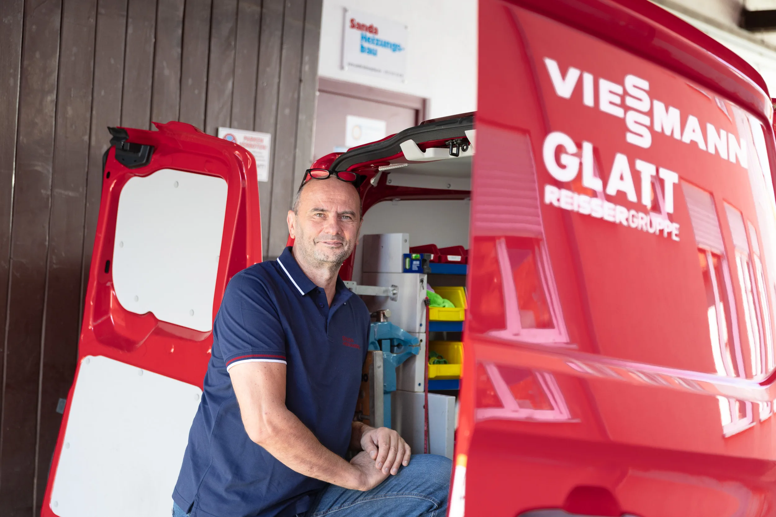 Silviu Sanda sitzt am geöffneten Heck des roten Servicewagens mit Viessmann- und Glatt-Beklebung, im Fahrzeug ordentlich sortiertes Werkzeug und Ersatzteile.